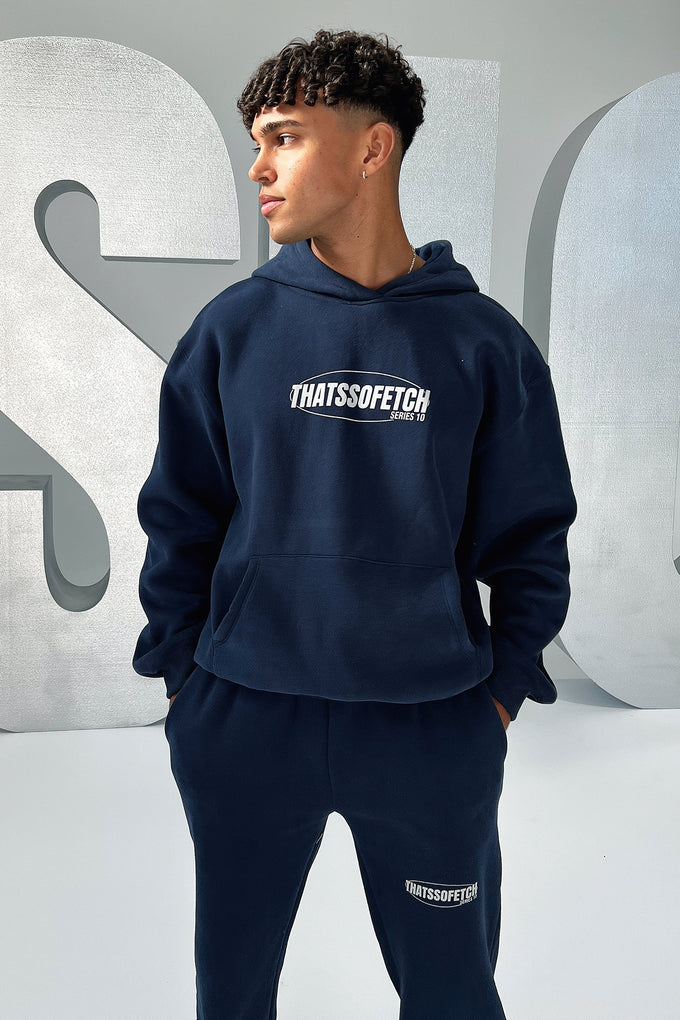 Person wearing a navy hoodie and pants with 'THATSSO Fetch' text, standing against a gray background with large letters.