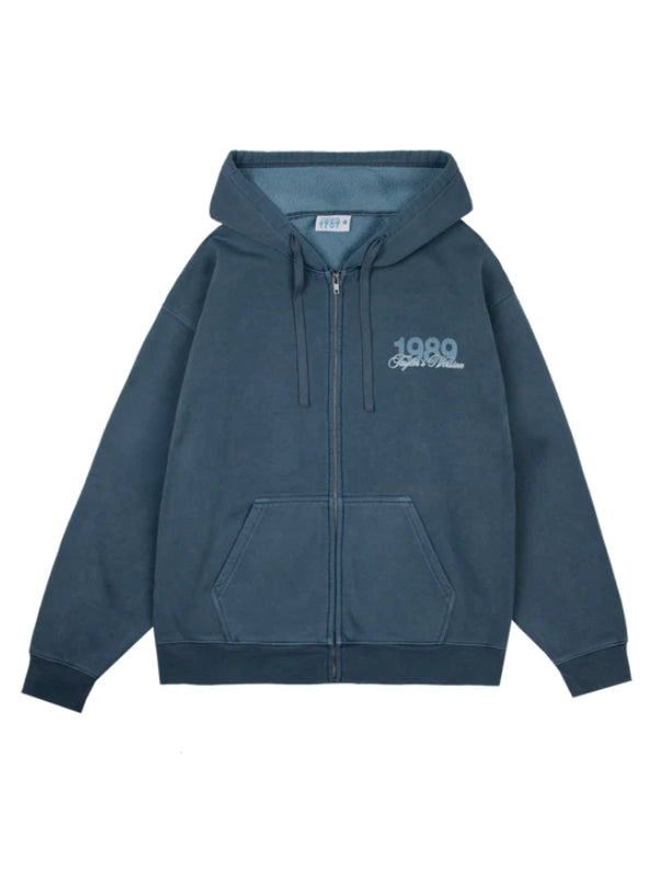 A slate blue zip-up hoodie with a drawstring hood, kangaroo pockets, and a light blue graphic print on the left chest reading '1980 Spirit of Williams'.