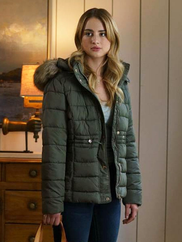 Woman wearing a green puffer jacket with fur hood in an indoor setting.